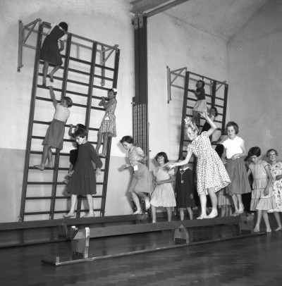 Klimmen op het wandrek en balanceren op de bank tijdens de gymles, Volkel 1955 (foto: Fotopersbureau Het Zuiden, collectie BHIC nr. 1672-003967) 