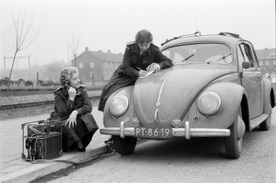 Twee vrouwelijke leden van BB bij een Volkswagen Kever. De ene bedient een veldtelefoon die is aangesloten (met kabels) op de Volkswagen; de ander vult op de motorkap een formulier in, Oss jaren 60 (foto: Daan Scholte, collectie Stadsarchief Oss nr. DSN1307_43416)