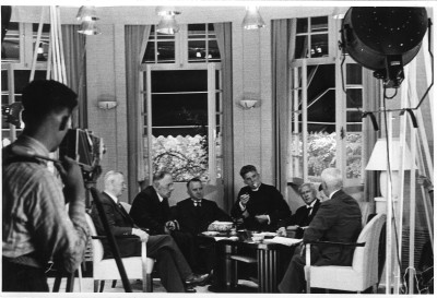 Werkfoto van opnames film Zonnelied, Etten 1938. Filmscène van de oprichtingsvergadering van het Wit-Gele Kruis in Overa met in het midden de pastoor, gespeeld door Ettens huisarts Chris Mol (foto: fotograaf onbekend, collectie Museum voor Verpleegkunde Culemborg)