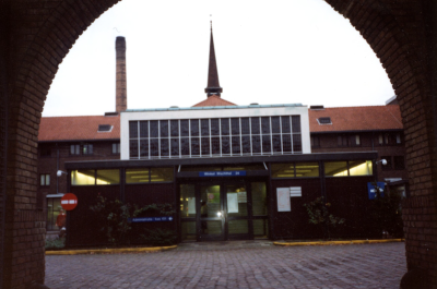 Zicht op ingang winkel en wachtruimte, daarboven de glas in lood raampartij van de kapel, 1990