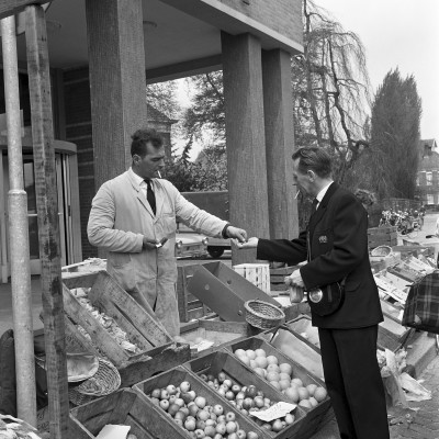 Marktmeester en gemeentebode Tini v.d. Kammen incasseert het markt- of staangeld van een kraamhouder op de markt voor het PTT postkantoor, Veghel ca. 1960 (foto: Harry van Liempd, collectie BHIC nr. 1915-001321)