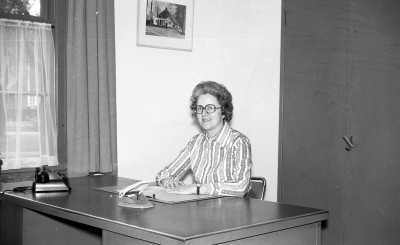 Vera de Kort zit als medewerkster van de gemeente achter haar bureau met papieren, perforator en telefoon, Vught (foto: collectie Vera Delleman-de Kort, collectie BHIC nr. 1923-004100)